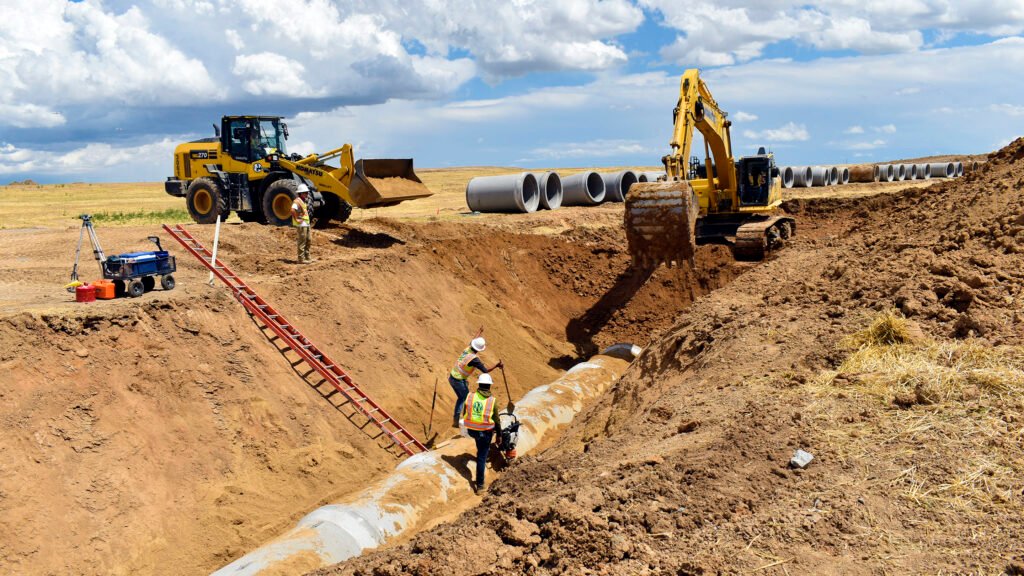 Nelson Pipeline employees assisting an excavator covering laid cement pipe in a ditch